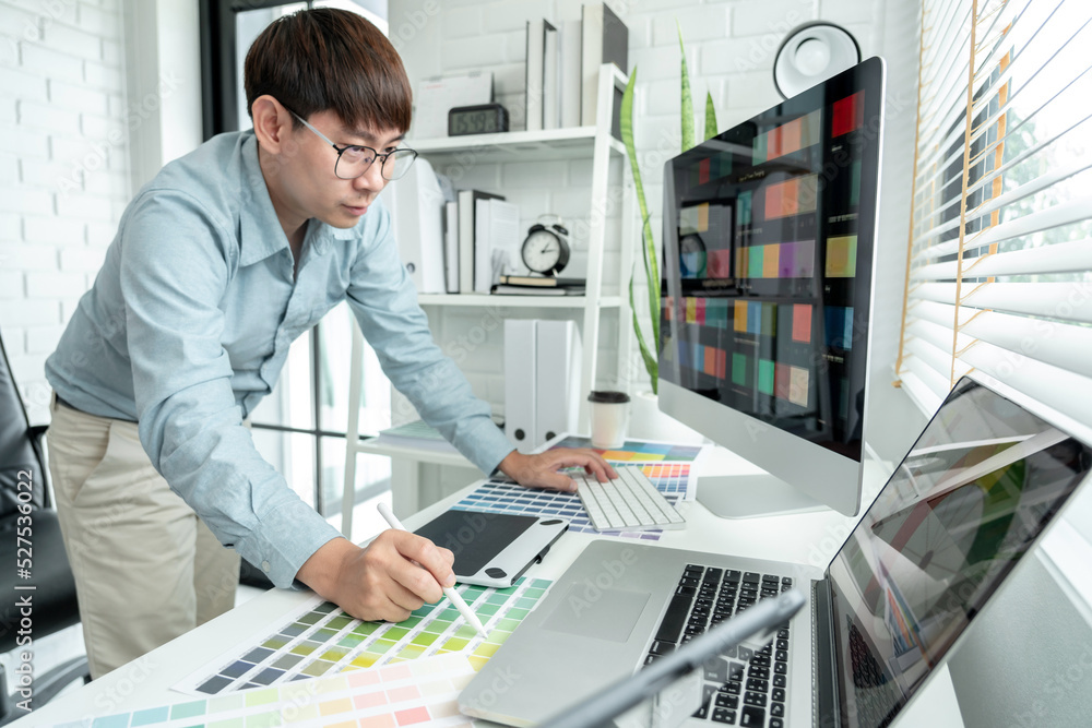 Poster male graphic designer is standing to choosing color swatch samples on multiple screens and working g