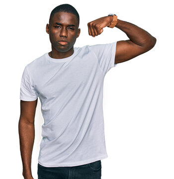 Young african american man wearing casual white t shirt strong person showing arm muscle, confident and proud of power