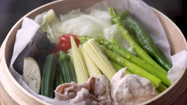 竹製のせいろから立ち上がる湯気と色鮮やかな夏野菜の蒸し料理 | オクラ、ヤングコーン、アスパラガス、豚肉が美しく盛り付けられたヘルシーな料理 | 蒸籠の蓋を開ける瞬間のシネマティックなフード映像 (Opening bamboo steamer with fresh summer vegetables and steam)