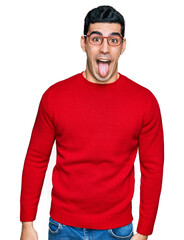 Handsome hispanic man wearing casual clothes and glasses sticking tongue out happy with funny...