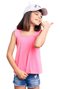 Young little girl with bang wearing funny kitty cap smiling with happy face looking and pointing to the side with thumb up.