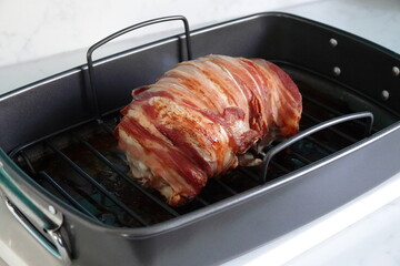 A turkey crown wrapped in Parma ham placed in a black baking tray in a kitchen. 