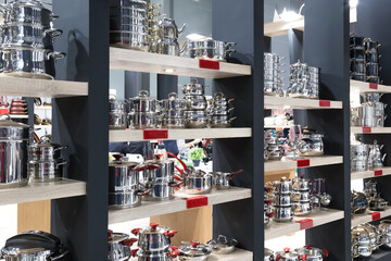 Shiny new stainless steel crockery and utensils, pots on open shelves. Department of kitchen utensils