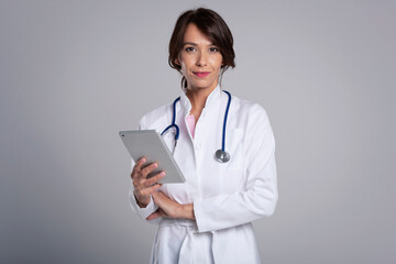 Smiling female doctor using digital table while standing at isolated grey background