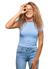 Beautiful caucasian teenager girl wearing casual clothes and glasses doing ok gesture with hand smiling, eye looking through fingers with happy face.