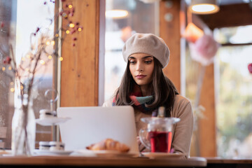 Smiling young woman sitting in cafe and using a laptop