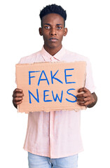 Young african american man holding fake news banner thinking attitude and sober expression looking...