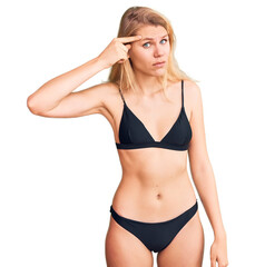 Young beautiful blonde woman wearing bikini pointing unhappy to pimple on forehead, ugly infection...