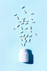 White pills fly out of bottle on blue background. Medicine, healthcare concept. Top view Flat lay