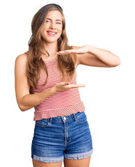 Fototapeta premium Beautiful caucasian young woman wearing casual clothes gesturing with hands showing big and large size sign, measure symbol. smiling looking at the camera. measuring concept.