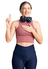 Beautiful caucasian young woman wearing gym clothes and using headphones smiling swearing with hand...