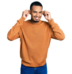 Fototapeta premium Young african american man wearing casual clothes smiling pulling ears with fingers, funny gesture. audition problem