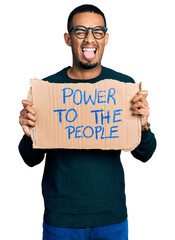 Young african american man holding power to the people banner sticking tongue out happy with funny expression.