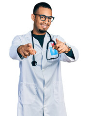 Young african american man wearing doctor uniform and stethoscope pointing to you and the camera with fingers, smiling positive and cheerful
