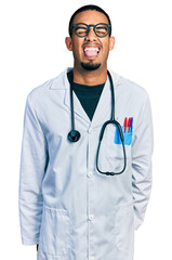 Fototapeta premium Young african american man wearing doctor uniform and stethoscope sticking tongue out happy with funny expression. emotion concept.
