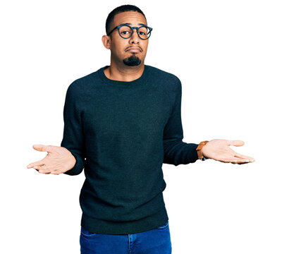 Young african american man wearing casual clothes and glasses clueless and confused expression with arms and hands raised. doubt concept. - Powered by Adobe