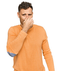 Young hispanic man wearing casual clothes smelling something stinky and disgusting, intolerable...