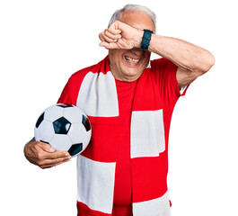 Senior man with grey hair football hooligan holding ball smiling cheerful playing peek a boo with...