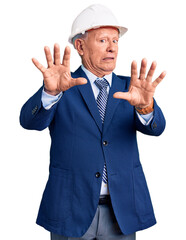 Senior handsome grey-haired man wearing suit and architect hardhat afraid and terrified with fear expression stop gesture with hands, shouting in shock. panic concept.