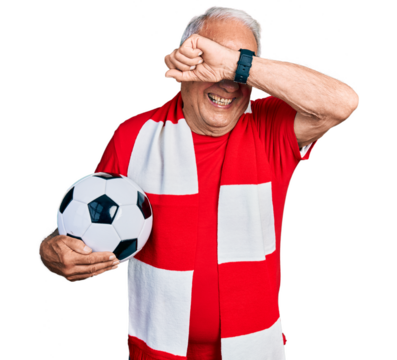 Senior man with grey hair football hooligan holding ball smiling cheerful playing peek a boo with hands showing face. surprised and exited - Powered by Adobe
