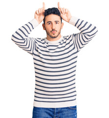 Young hispanic man wearing casual clothes doing funny gesture with finger over head as bull horns