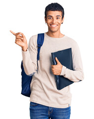 Young african amercian man wearing student backpack holding binder smiling happy pointing with hand and finger to the side - obrazy, fototapety, plakaty