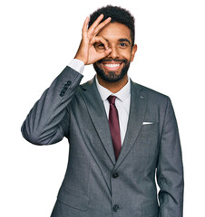Young african american man wearing business clothes doing ok gesture with hand smiling, eye looking through fingers with happy face.