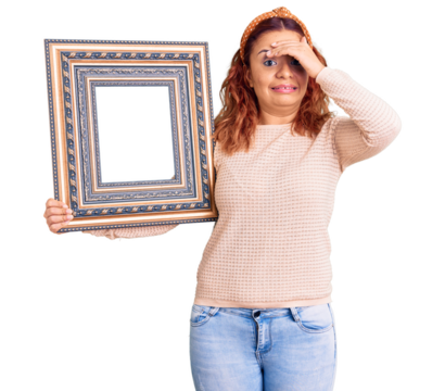 Young latin woman holding empty frame stressed and frustrated with hand on head, surprised and angry face