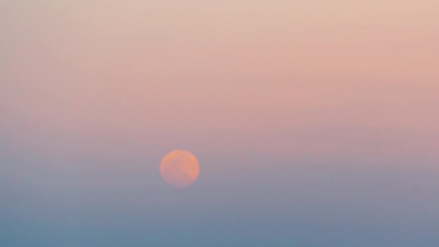 The full moon is setting in the sunset sky. 4K time-lapse 