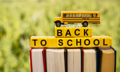 Realistic yellow school bus toy standing on stack of books. back to school lettering. blurred green...