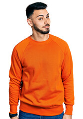 Fototapeta premium Young hispanic man with beard wearing casual orange sweater smiling looking to the side and staring away thinking.