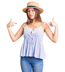 Obraz na płótnie Canvas Beautiful brunette young woman wearing summer hat looking confident with smile on face, pointing oneself with fingers proud and happy.
