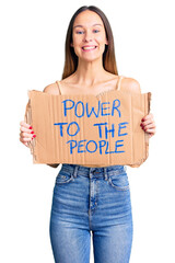 Beautiful brunette young woman holding power to the people banner looking positive and happy standing and smiling with a confident smile showing teeth