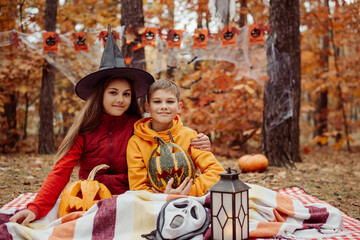 Happy children, boy and girl, in autumn forest. Halloween decoration, festive atmosphere, warm orange colours of the leaves.