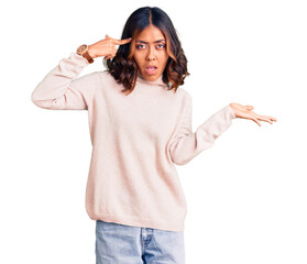 Young beautiful mixed race woman wearing winter turtleneck sweater confused and annoyed with open palm showing copy space and pointing finger to forehead. think about it.