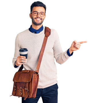 Young handsome hispanic man wearing leather bag and drinking take away coffee smiling happy pointing with hand and finger to the side