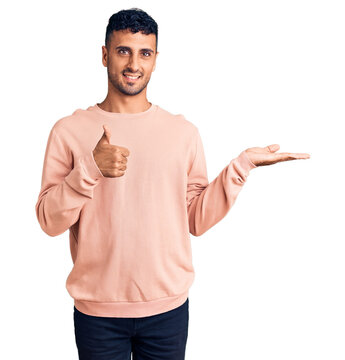 Young hispanic man wearing casual clothes showing palm hand and doing ok gesture with thumbs up, smiling happy and cheerful