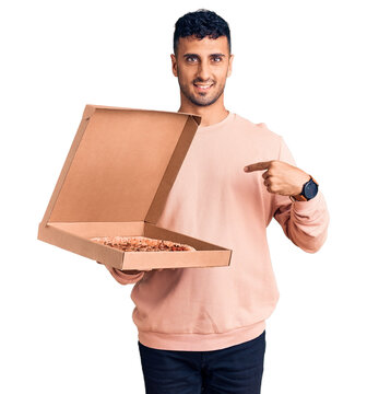 Young hispanic man holding delivery pizza box pointing finger to one self smiling happy and proud