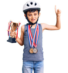 Little cute boy kid wearing bike helmet and winner medals holding winner trophy surprised with an...
