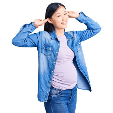 Young Beautiful Chinese Woman Pregnant Expecting Baby Smiling Pulling Ears With Fingers, Funny Gesture. Audition Problem