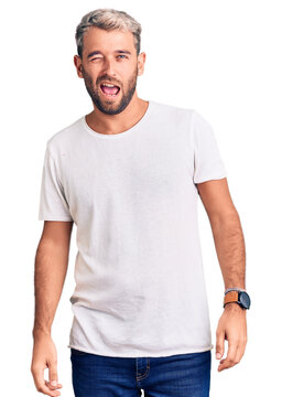 Young handsome blond man wearing casual t-shirt winking looking at the camera with sexy expression, cheerful and happy face.