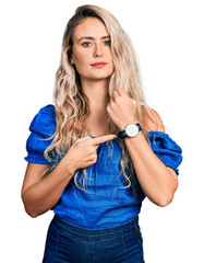 Young blonde woman wearing casual clothes in hurry pointing to watch time, impatience, looking at...