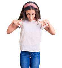 Cute hispanic child girl wearing casual white tshirt pointing down with fingers showing...