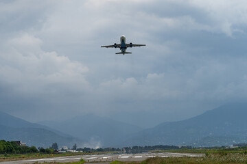Fototapeta na wymiar Airplane taking off from the airport, mountains on background. Passenger plane fly up over take-off runway. Trip, flight, travel concept