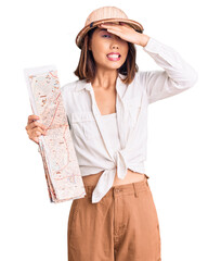 Young beautiful chinese girl wearing explorer hat holding map stressed and frustrated with hand on head, surprised and angry face