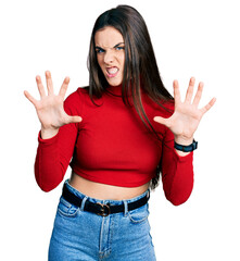 Young brunette teenager wearing red turtleneck sweater smiling funny doing claw gesture as cat, aggressive and sexy expression