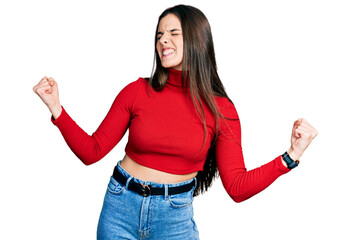 Young brunette teenager wearing red turtleneck sweater very happy and excited doing winner gesture...