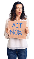 Young beautiful hispanic woman holding act now banner scared and amazed with open mouth for surprise, disbelief face