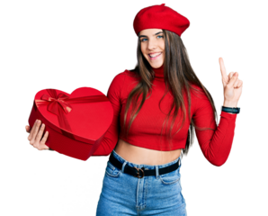 Young brunette teenager holding heart draw smiling with an idea or question pointing finger with happy face, number one