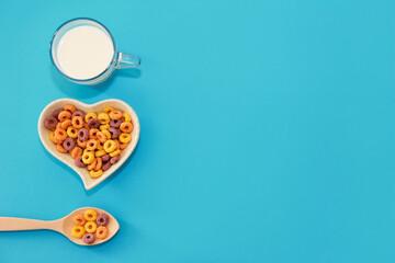 children's dry breakfast multicolored rings in a plate and a wooden spoon, next to a white milk drink in a transparent mug